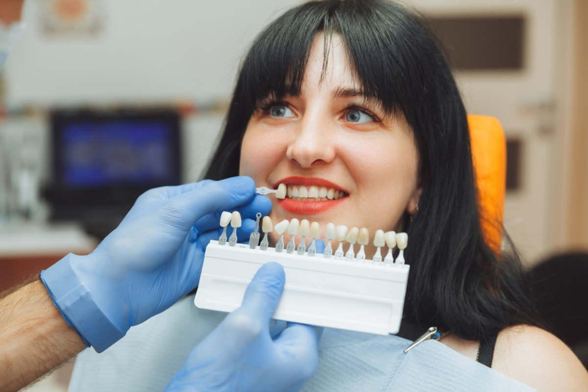 Choosing Veneers Woman examining dental shade guide samples in dental office with equipment visible in background.